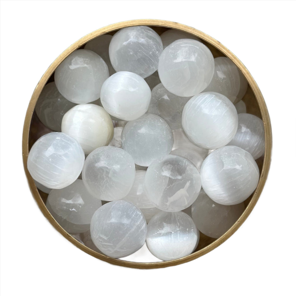 Round selenite tumbled stones in a wooden bowl for meditation and spiritual clarity.